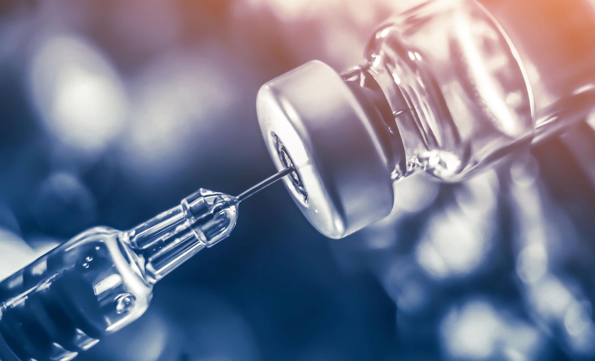 A syringe is being inserted into a bottle of vaccine.