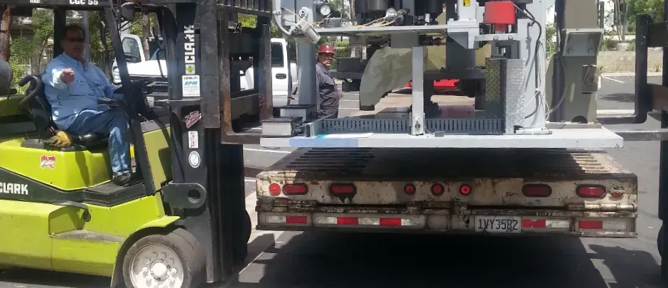 A man is driving a forklift down a street next to a truck.