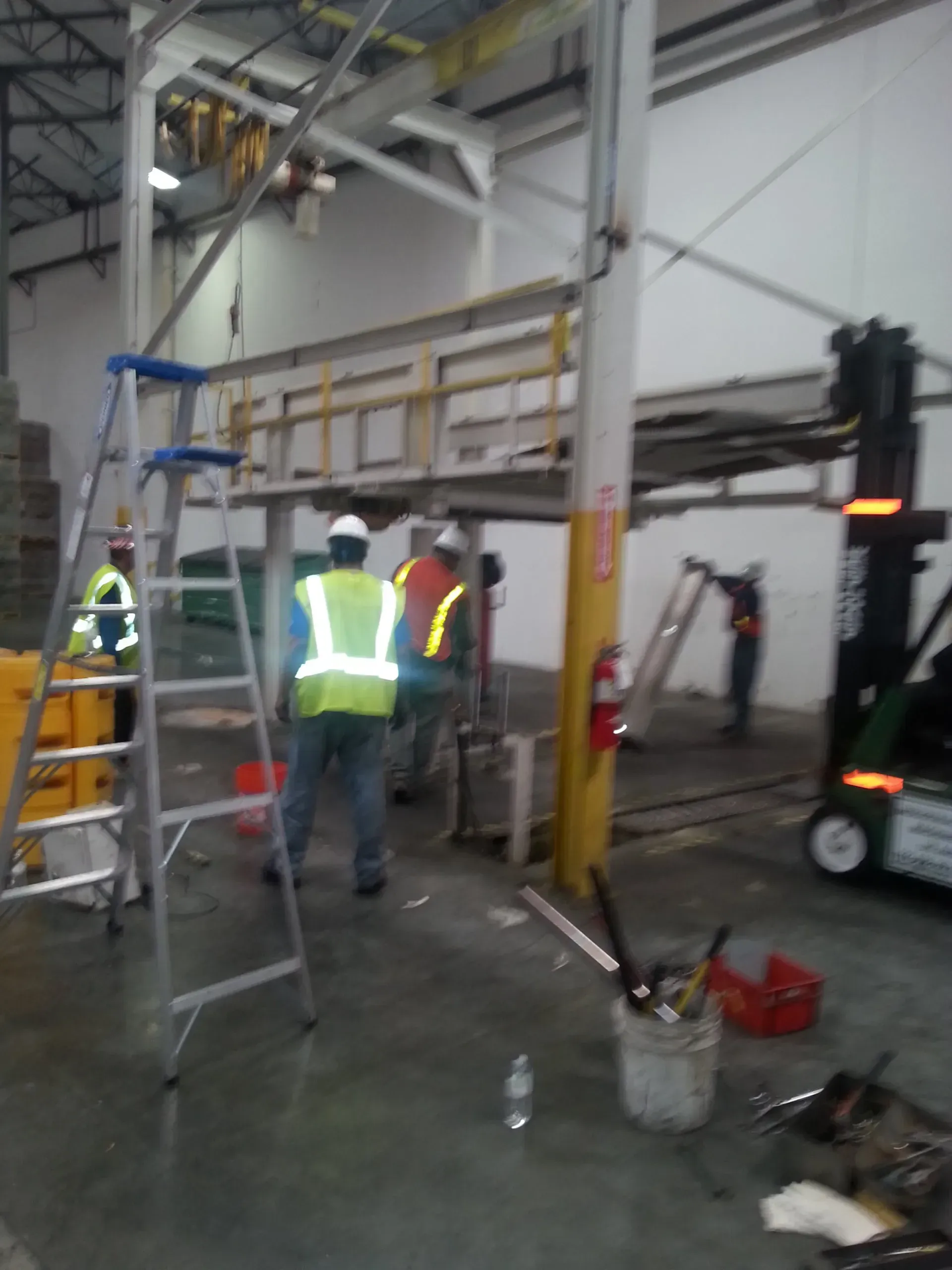 A group of men are working in a warehouse with a forklift in the background.