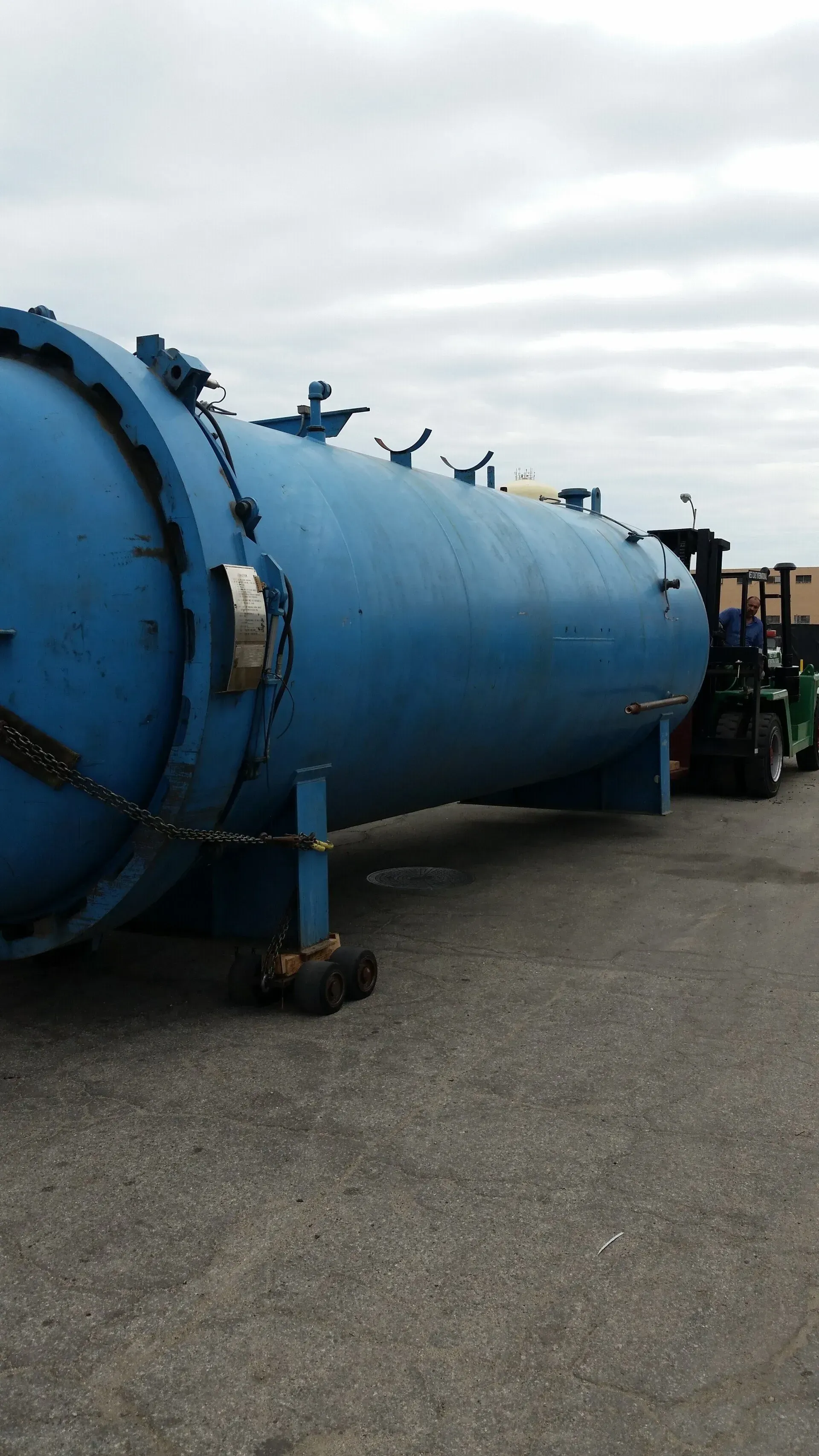 A large blue tank is sitting in a parking lot next to a forklift.