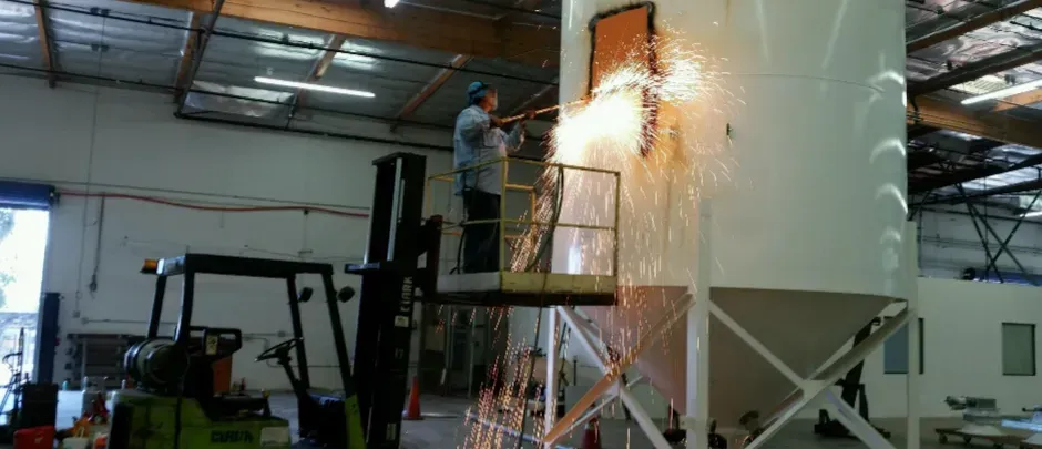 A man is standing on a ladder next to a forklift in a factory.