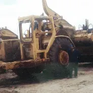 A man is standing next to a large yellow bulldozer in a dirt field.