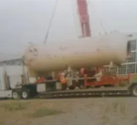 A large tank is being lifted by a crane on a trailer.