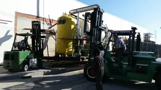 A green forklift is carrying a large yellow tank
