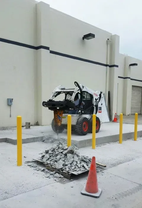 A bobcat is cutting concrete in front of a building