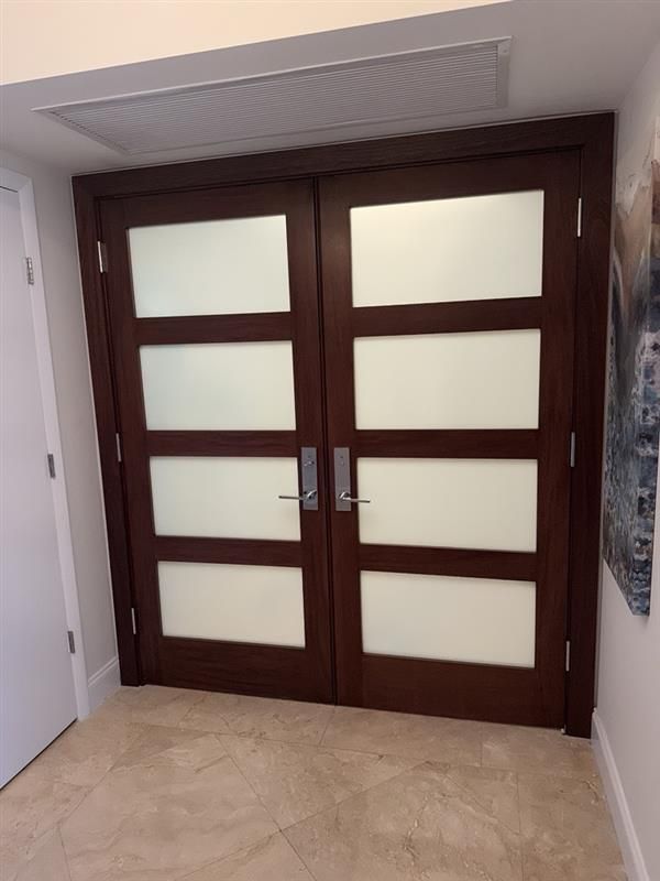 A gray door with a slatted center panel in a concrete room. Red pipe is above.