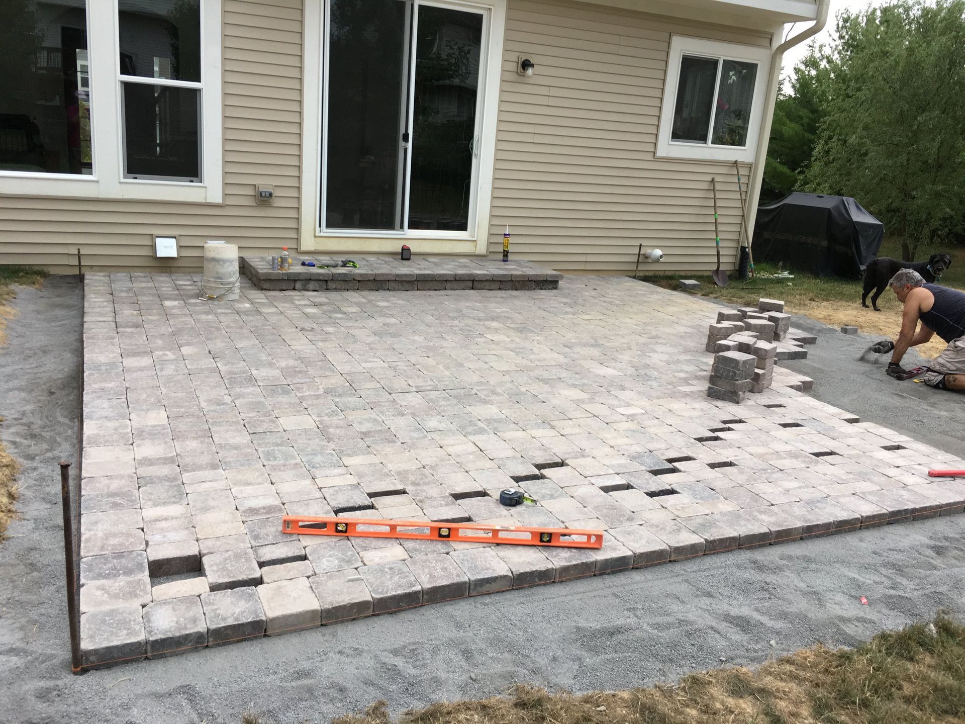 A man is laying bricks on a patio in front of a house.