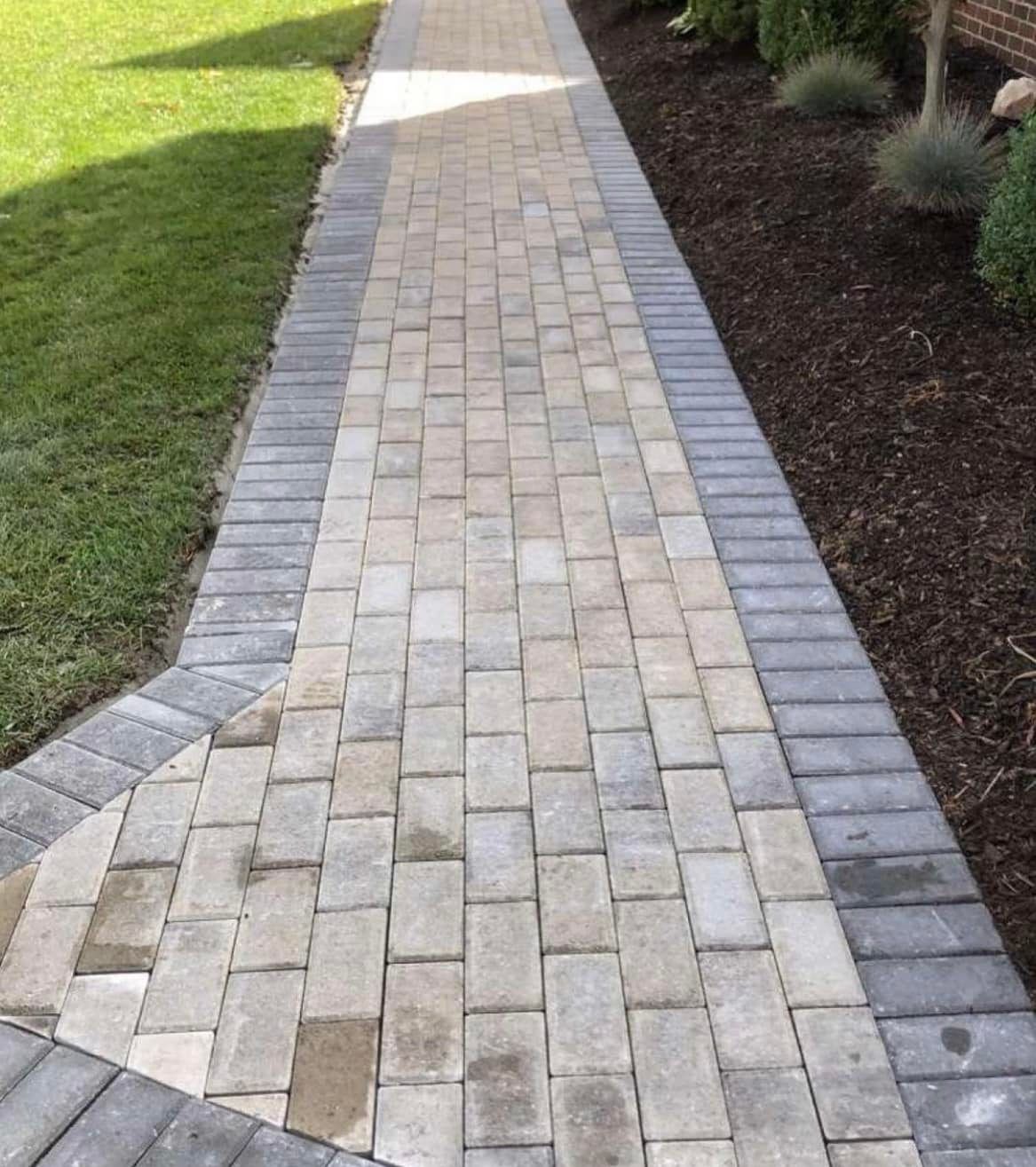 A brick walkway leading to a lush green lawn.