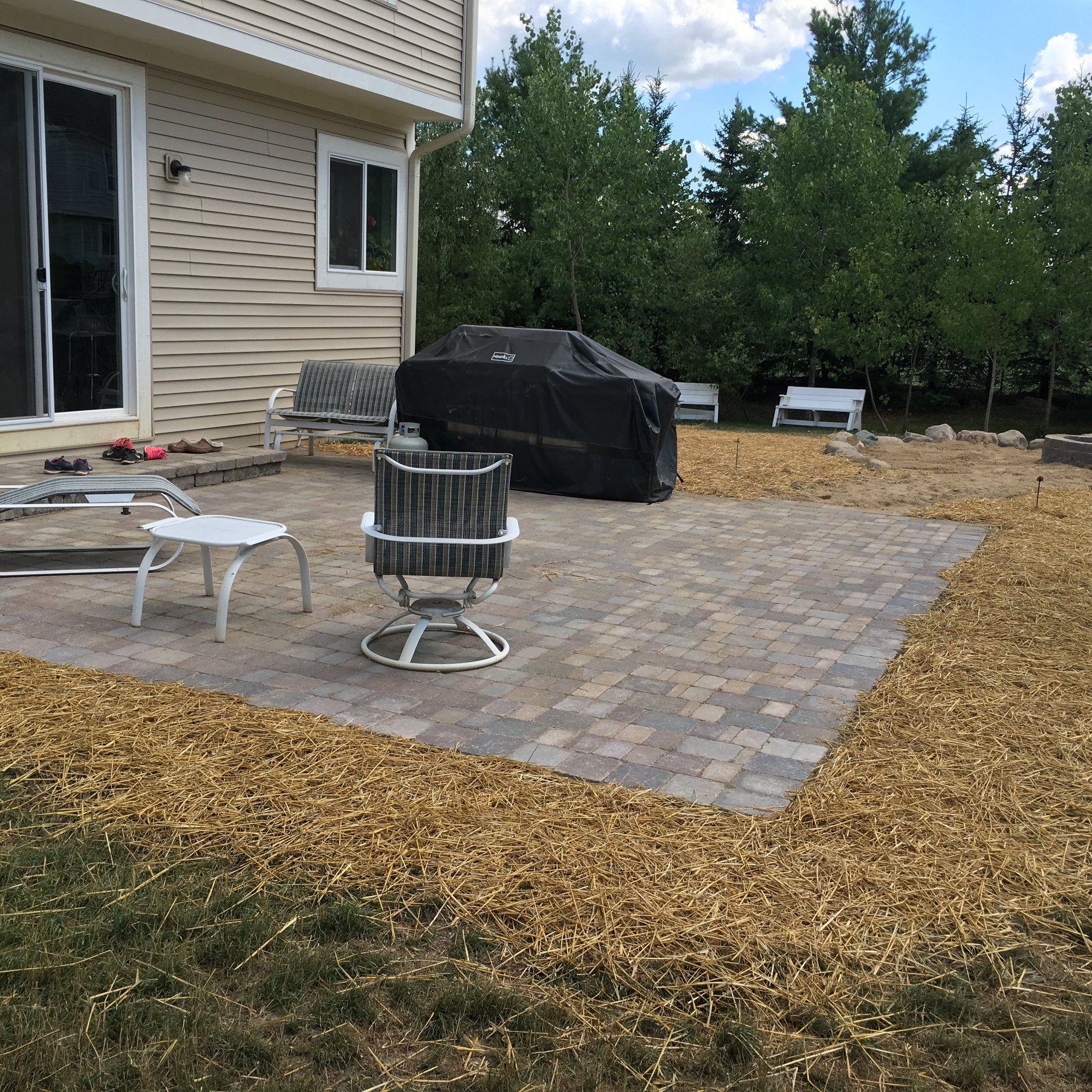 A patio with a grill and chairs in front of a house.