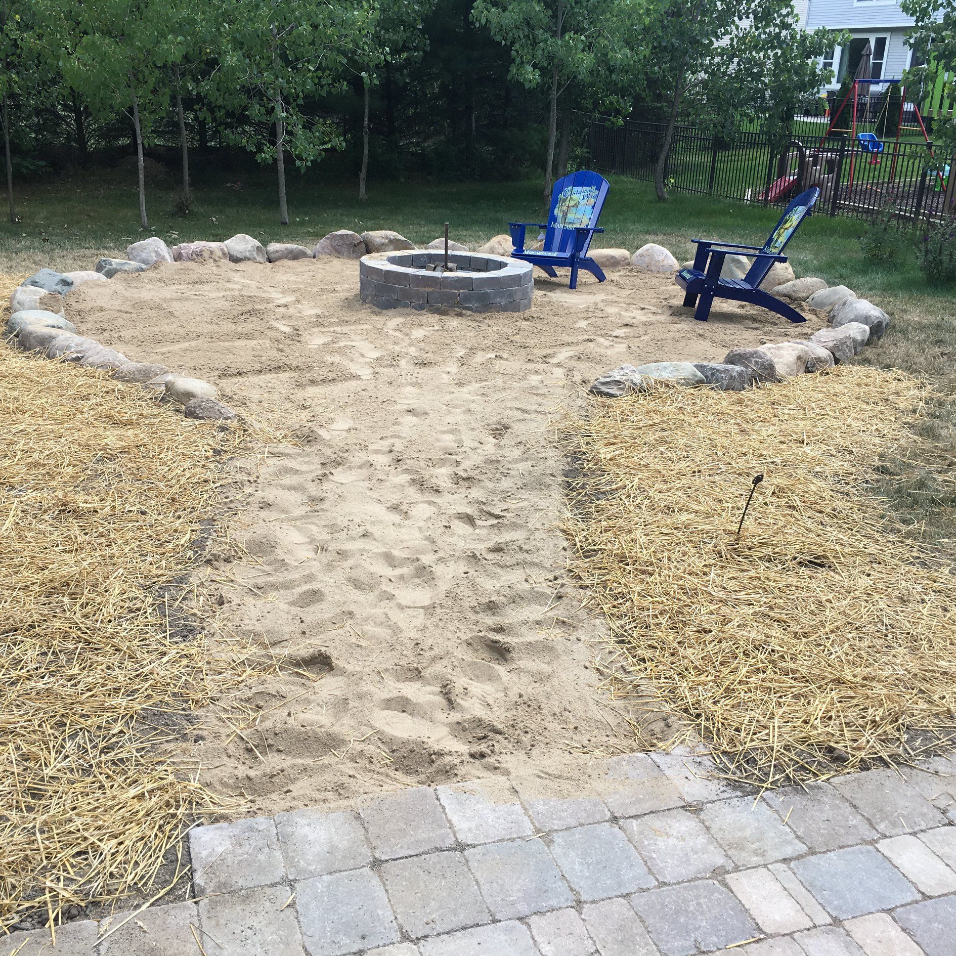 There is a fire pit in the middle of the yard surrounded by chairs.