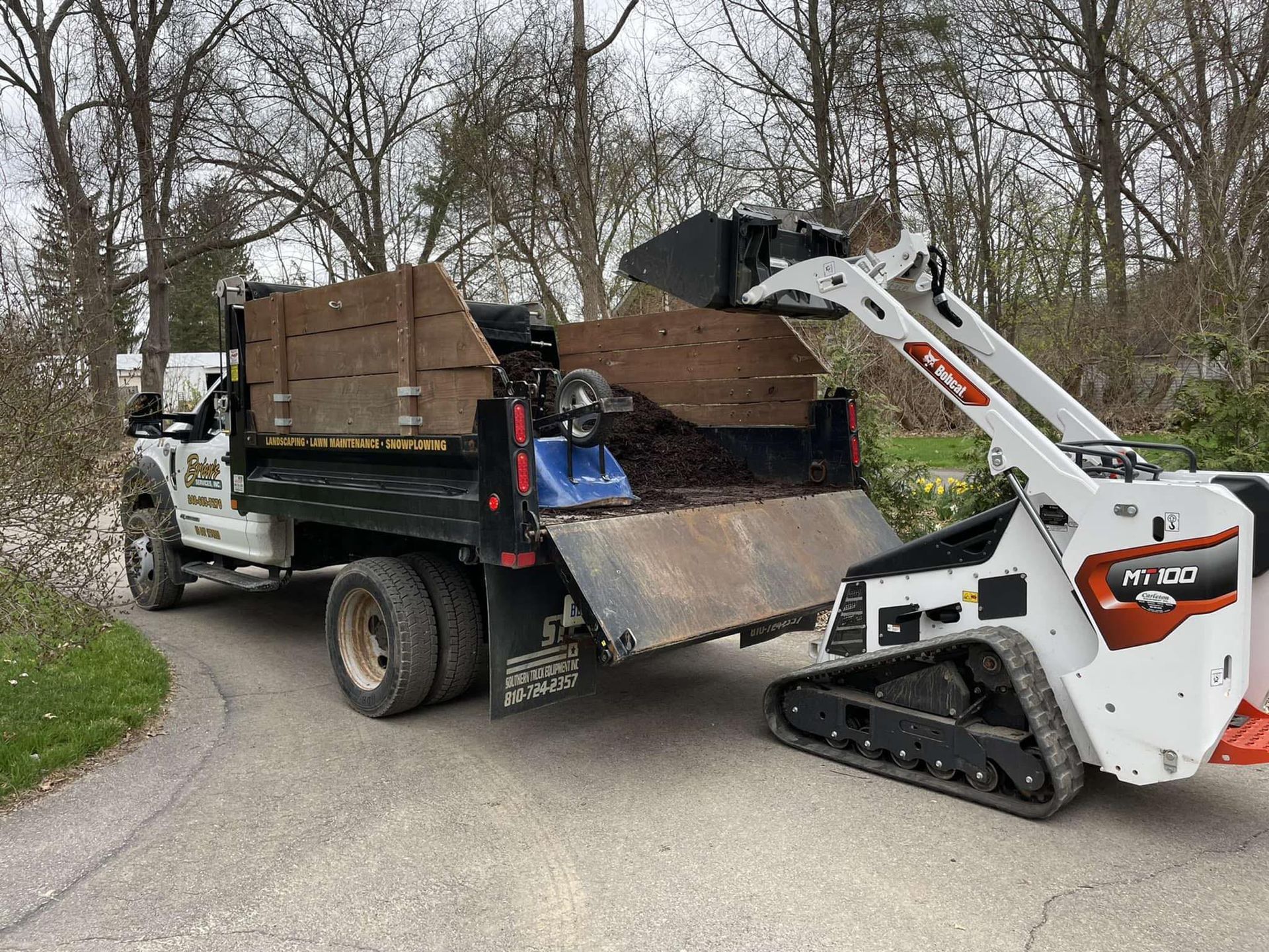 A dump truck is being towed by a skid steer loader.