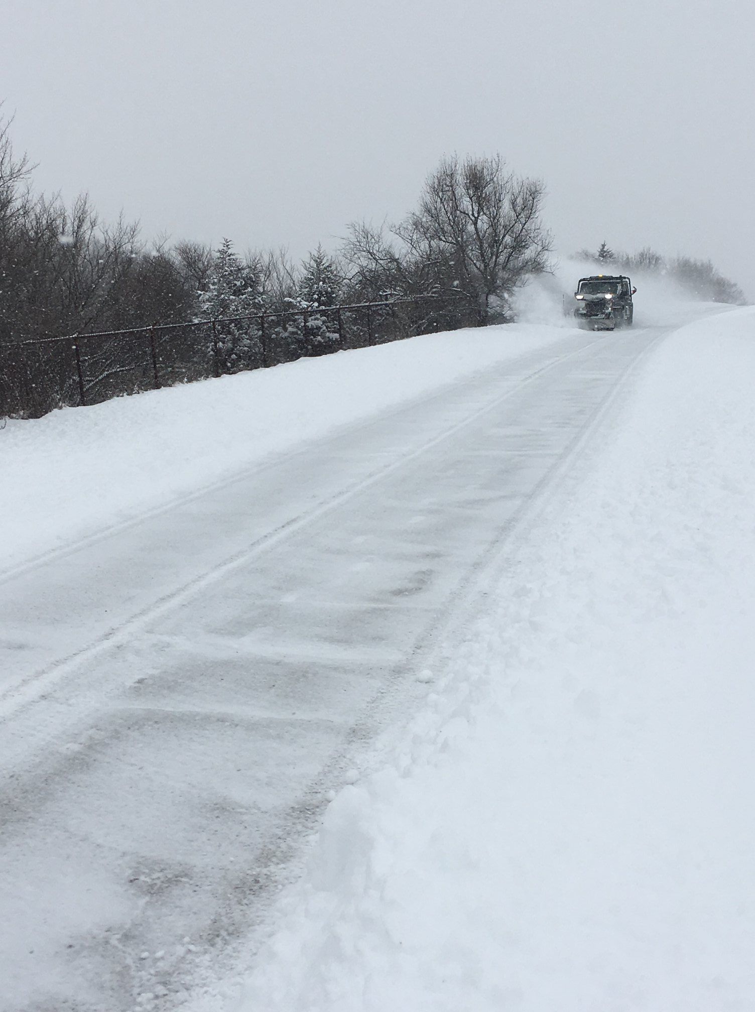 A truck is driving down a snow covered road.