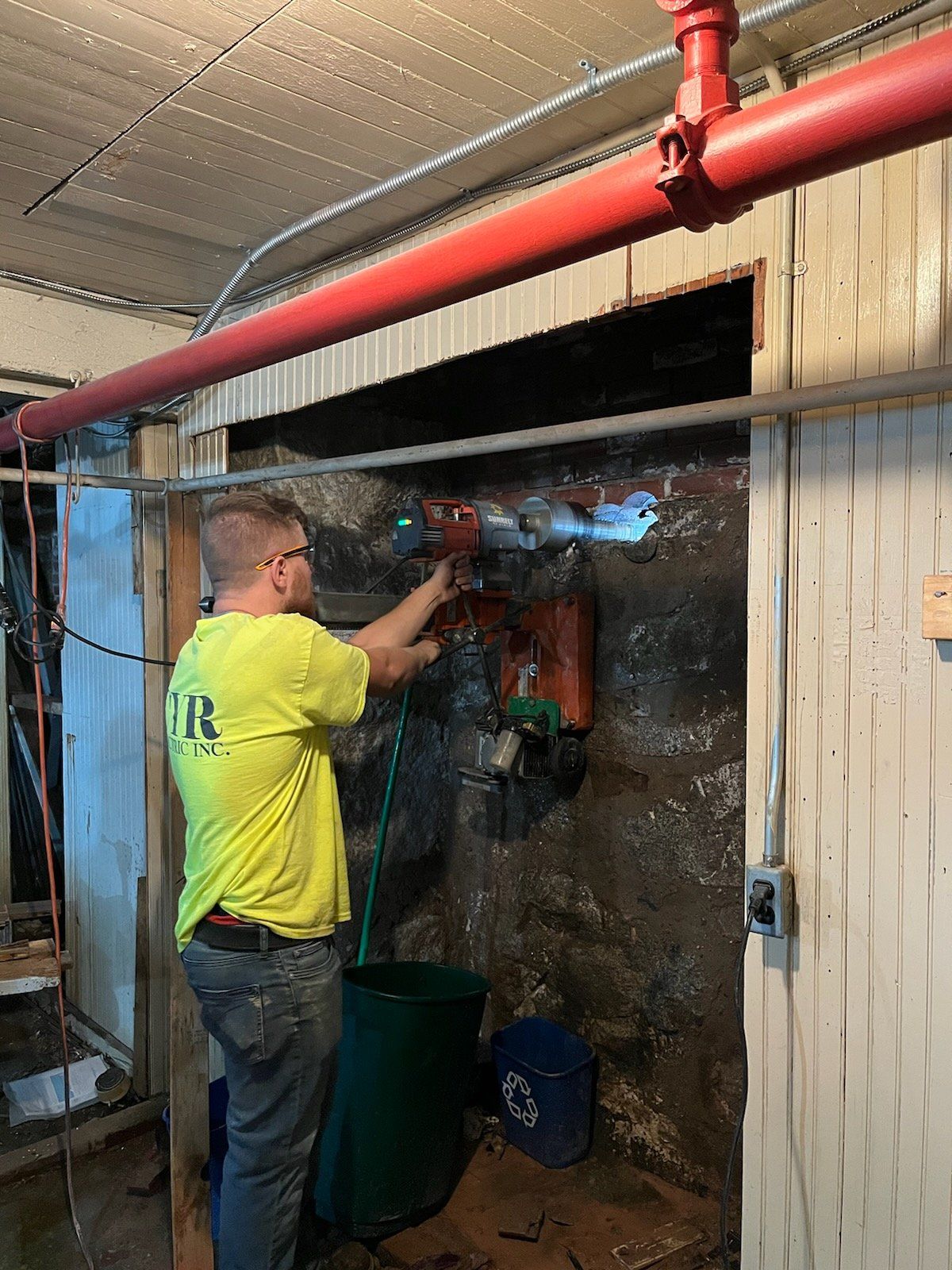 A man in a yellow shirt is working on a pipe in a basement.