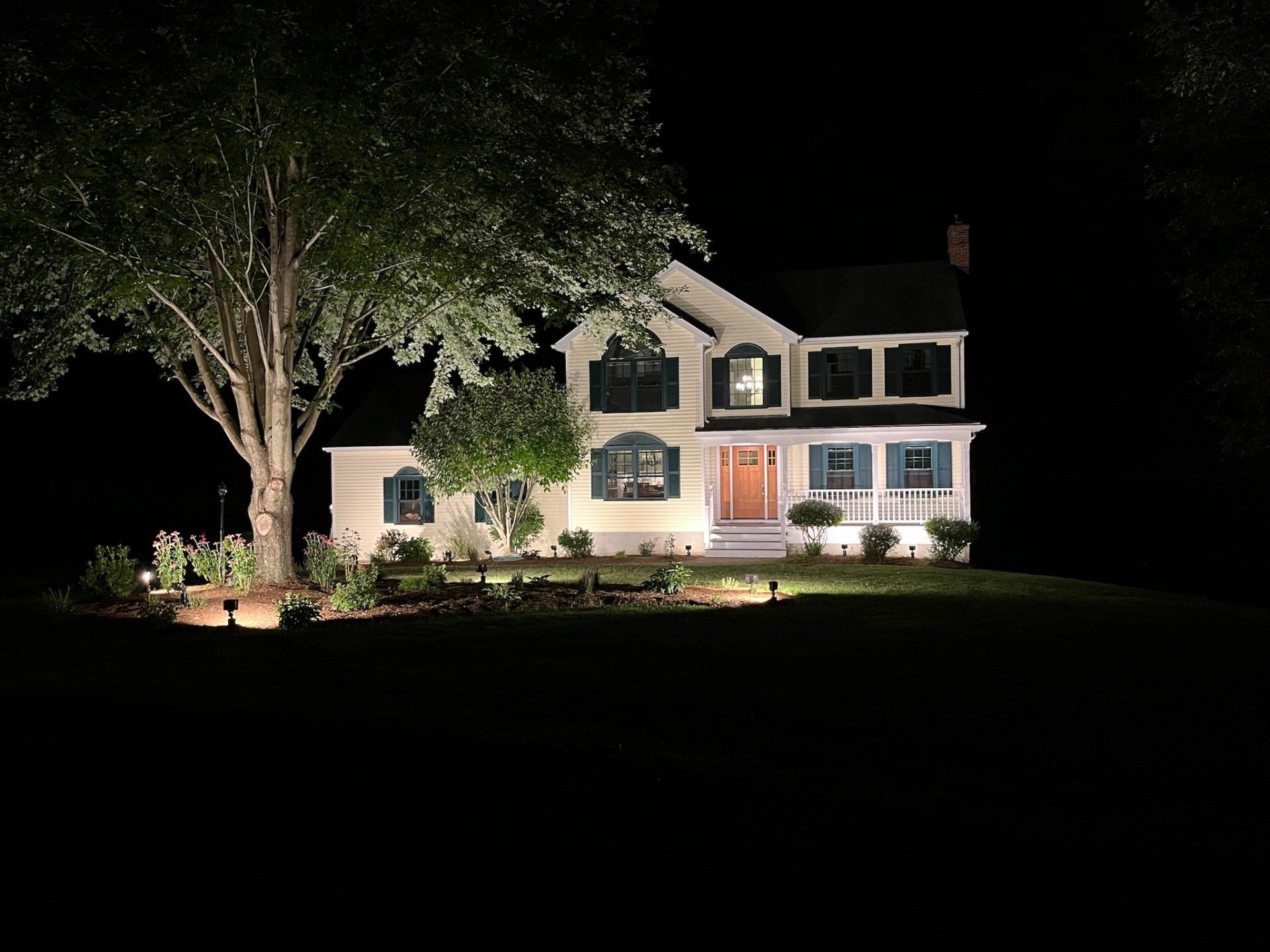 A house is lit up at night with a tree in front of it.