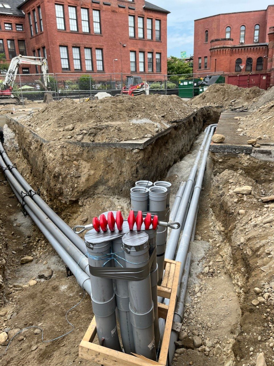 A bunch of pipes are laying in the dirt in front of a brick building