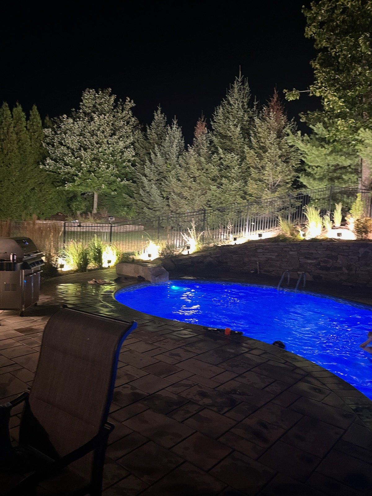 A large swimming pool is lit up at night surrounded by trees.