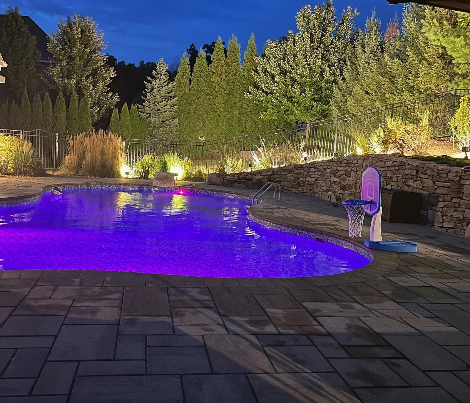 A large swimming pool is lit up with purple lights at night