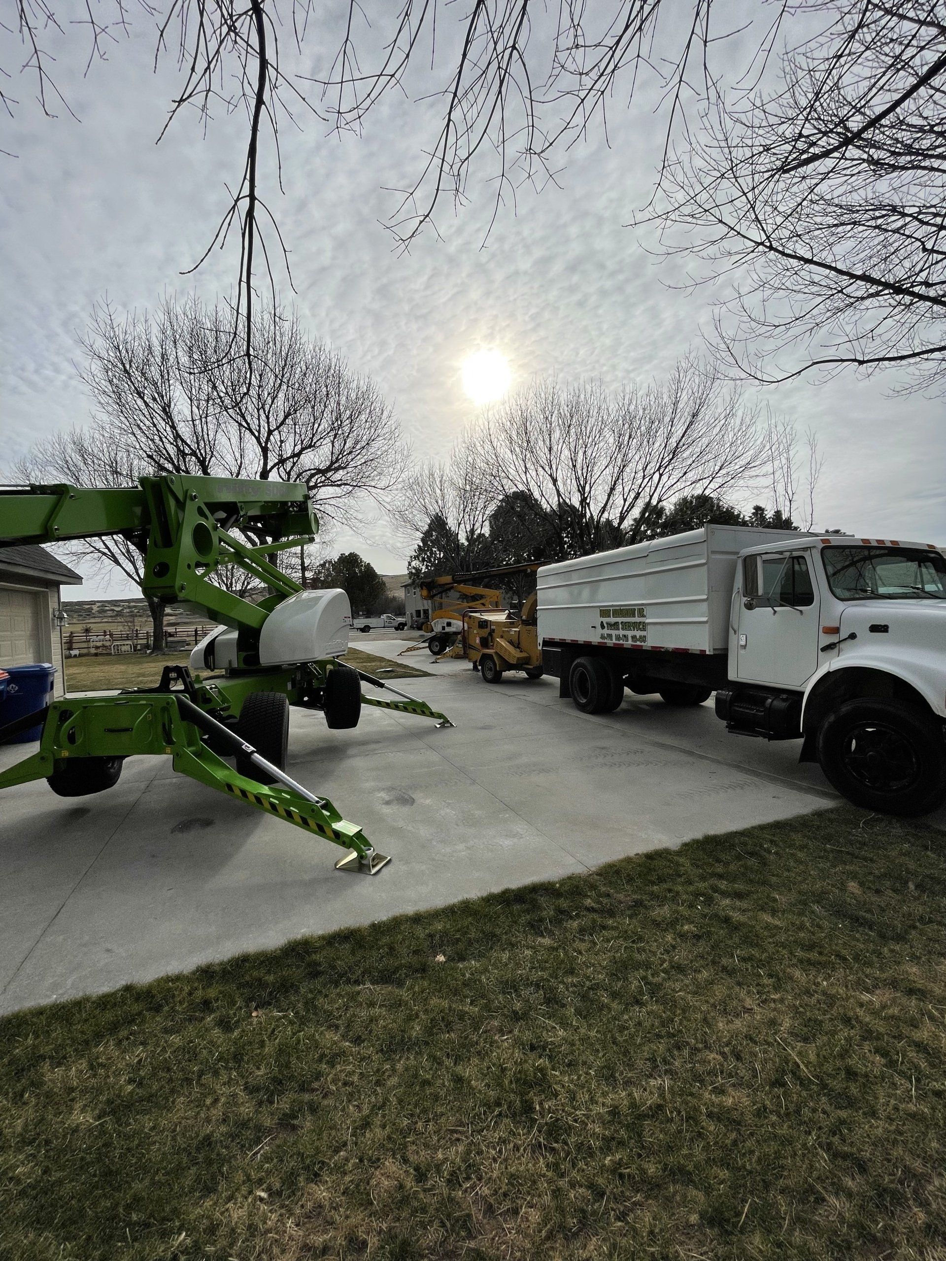 A green crane is parked next to a white truck in a driveway.