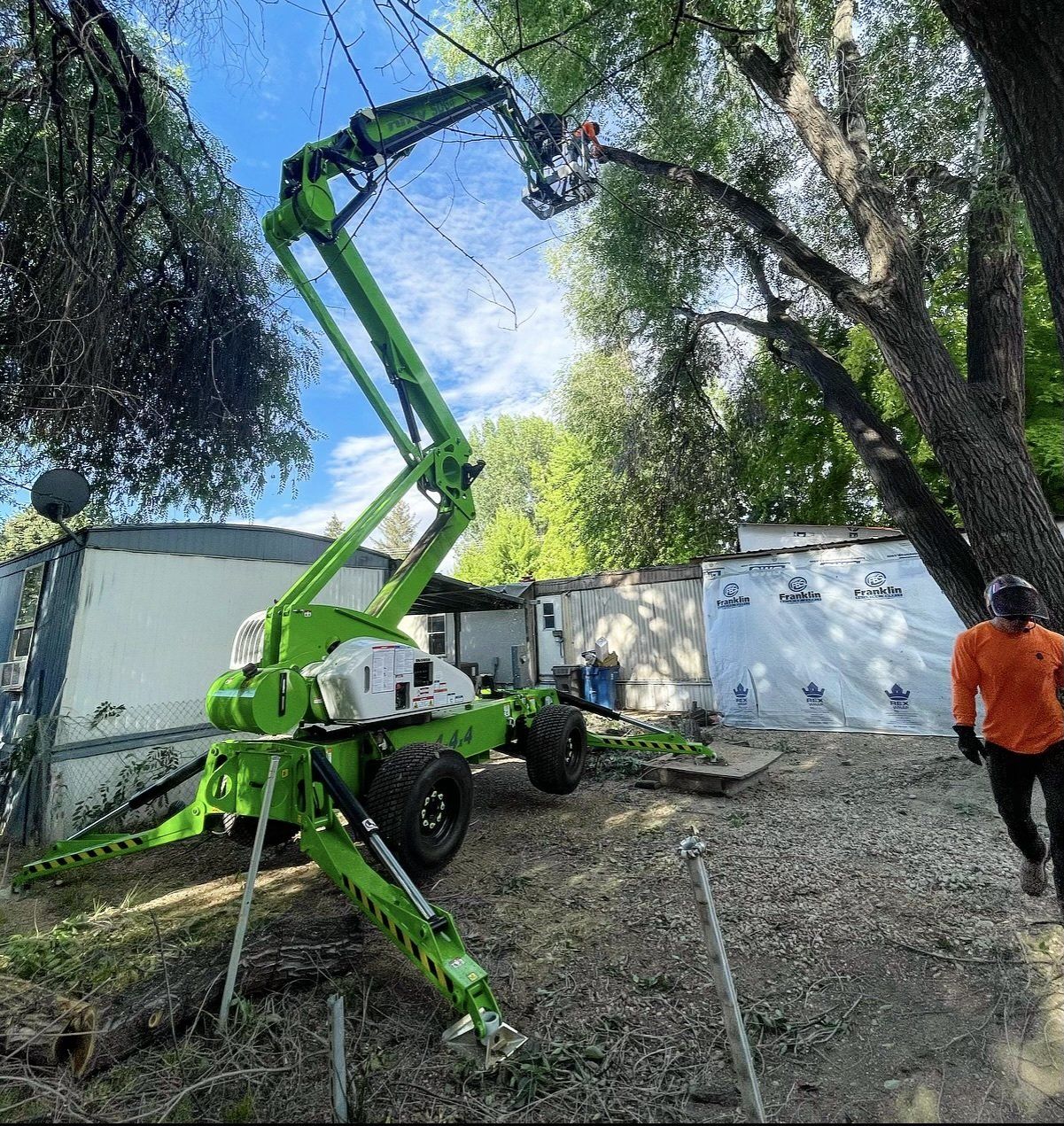 A man is standing next to a green crane that is cutting a tree.
