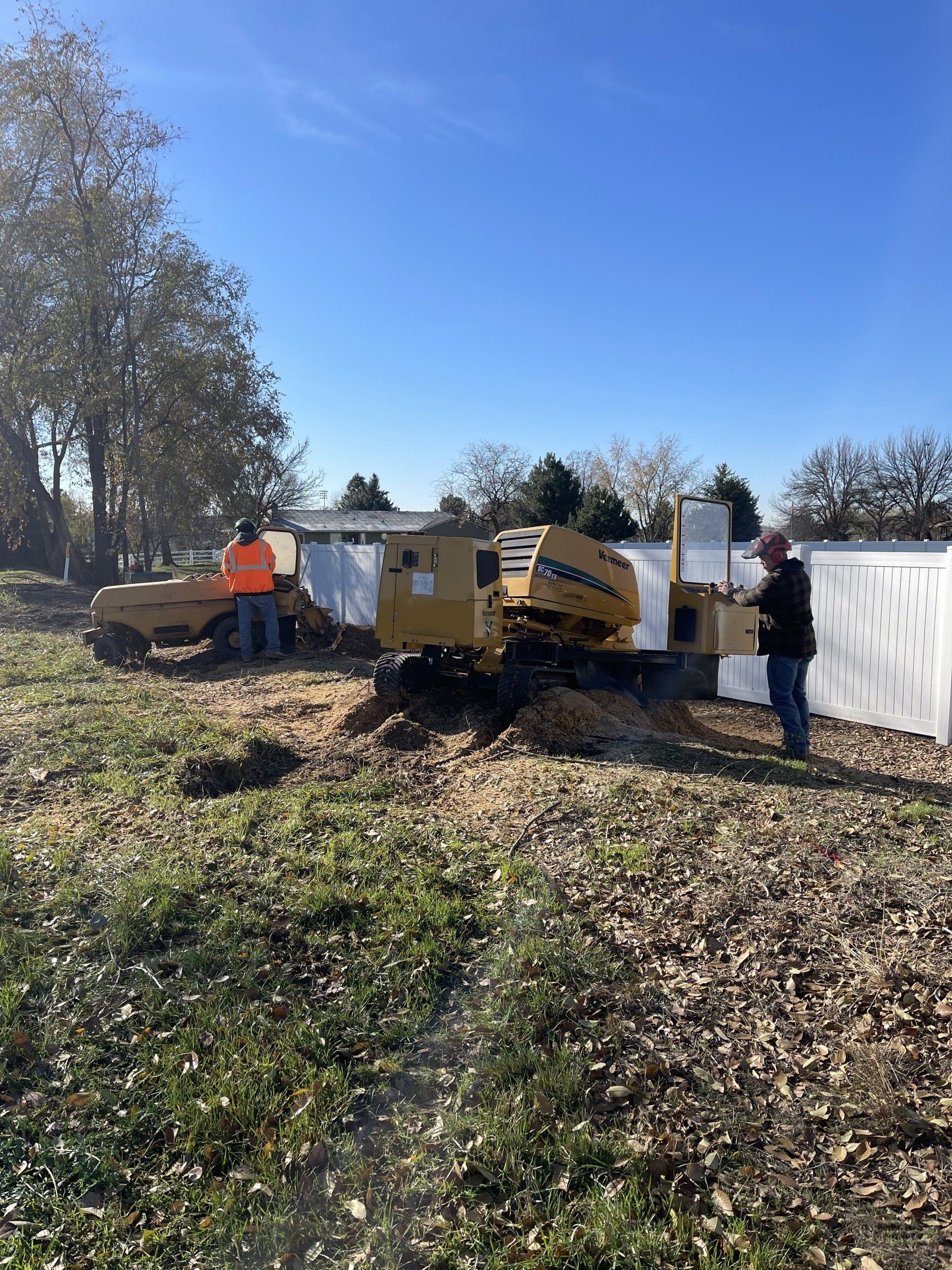 Two men are working on a stump grinder in a field.