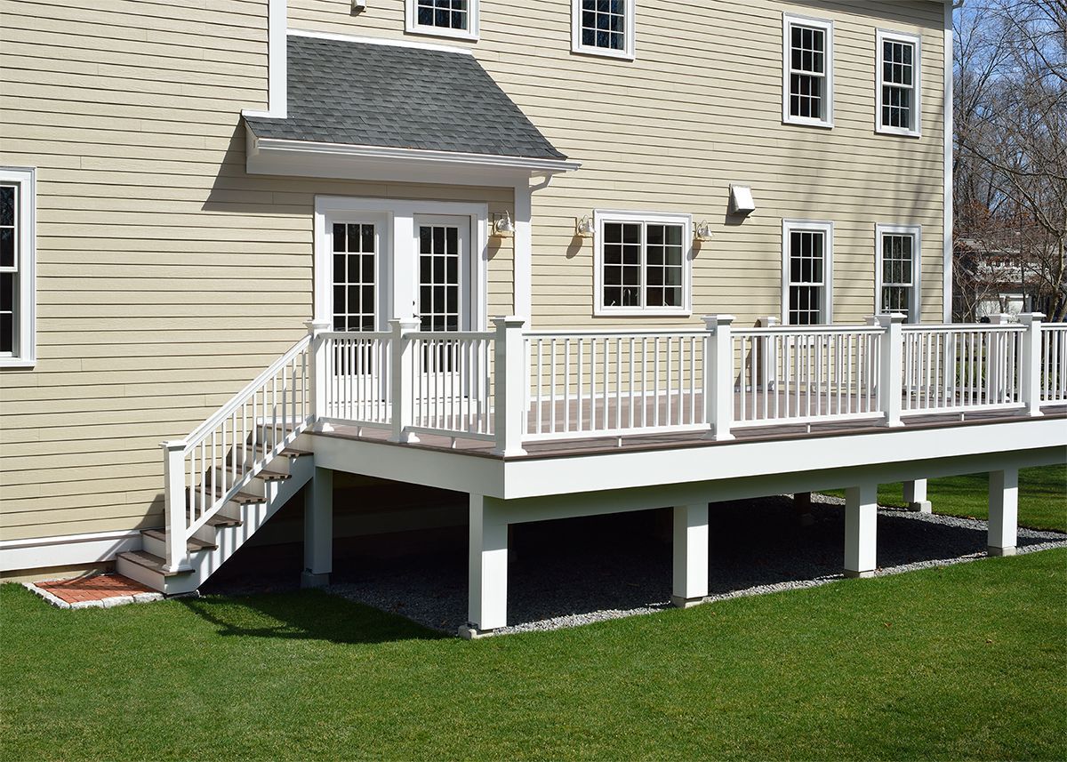 A house with a white deck and stairs leading down to a grassy yard.