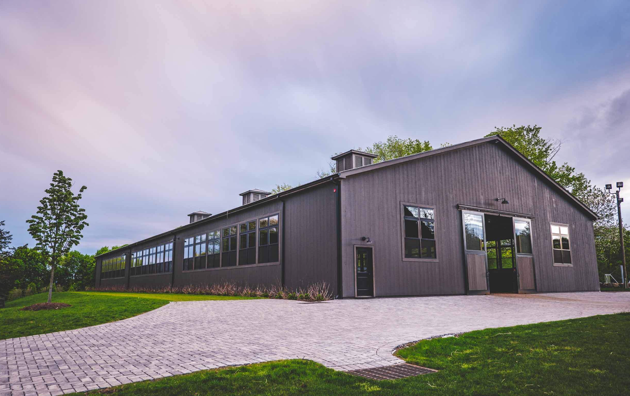 Modern gray barn-style building with large windows, a stone path, and green grass under a cloudy sky.