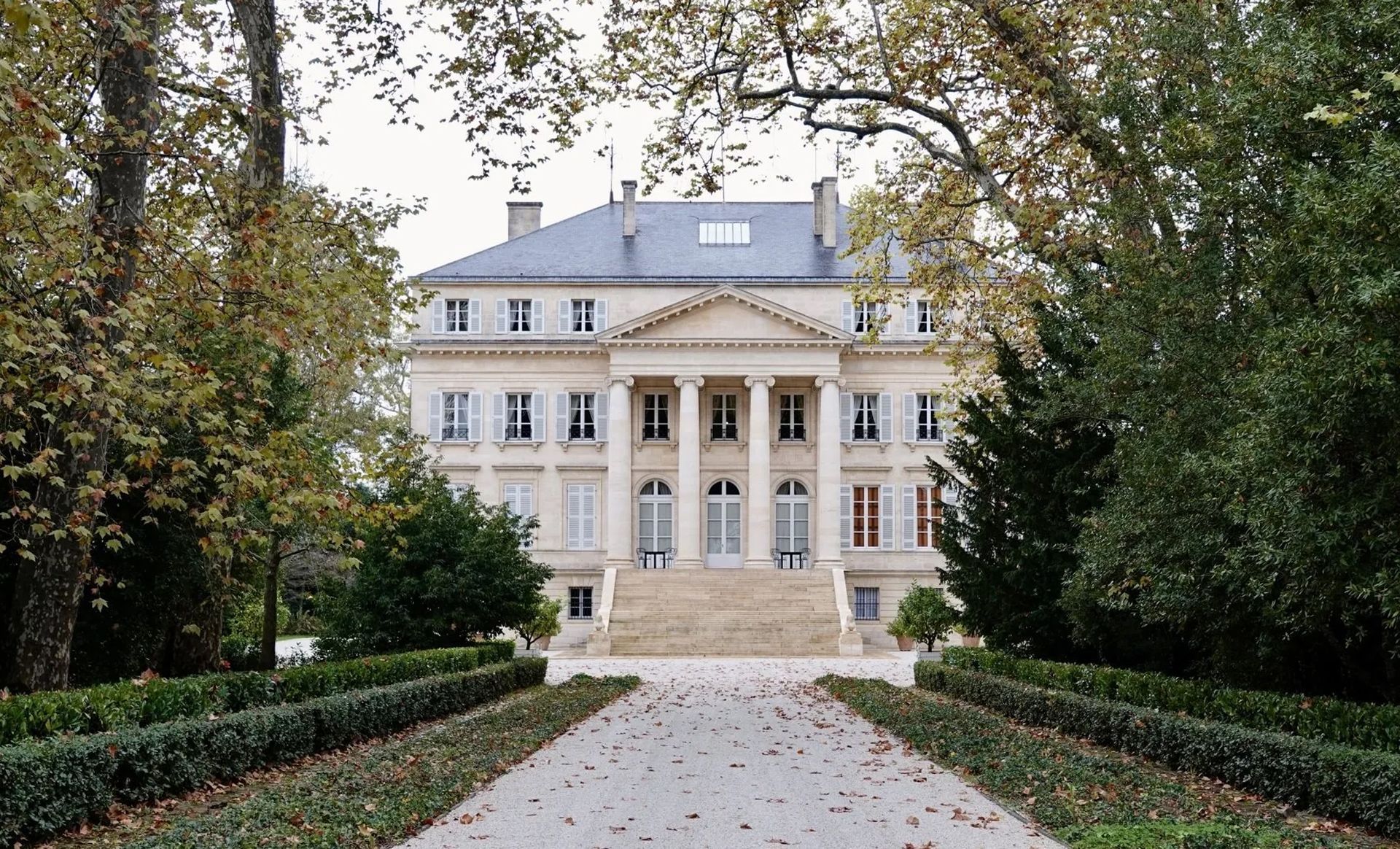A large white building with columns is surrounded by trees and bushes