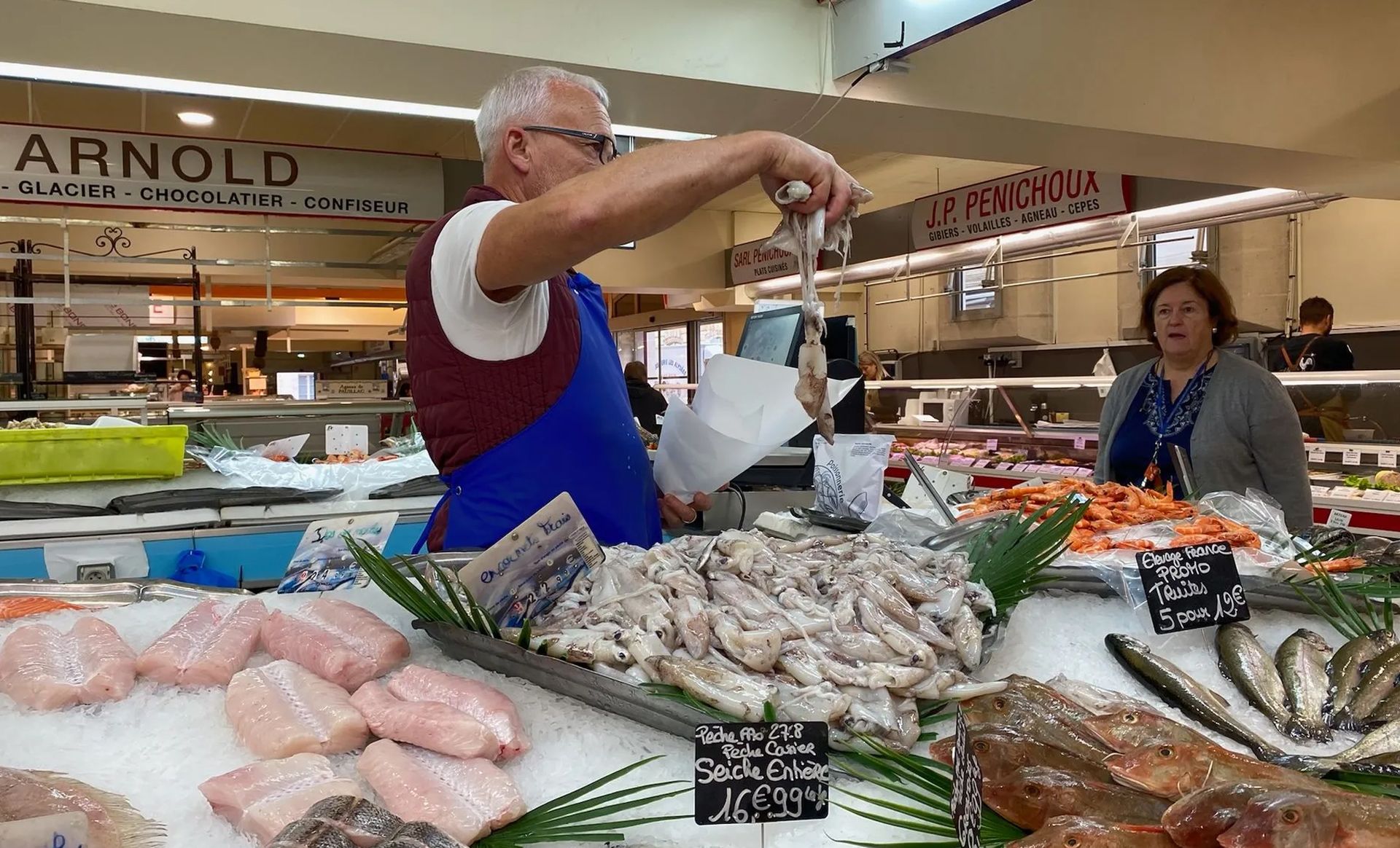 A man is standing in front of a display of seafood in a market.