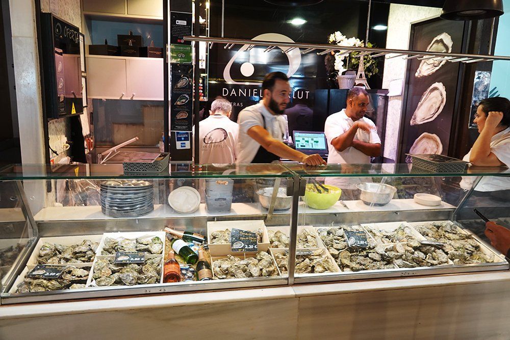 A man is standing behind a glass display case filled with oysters.