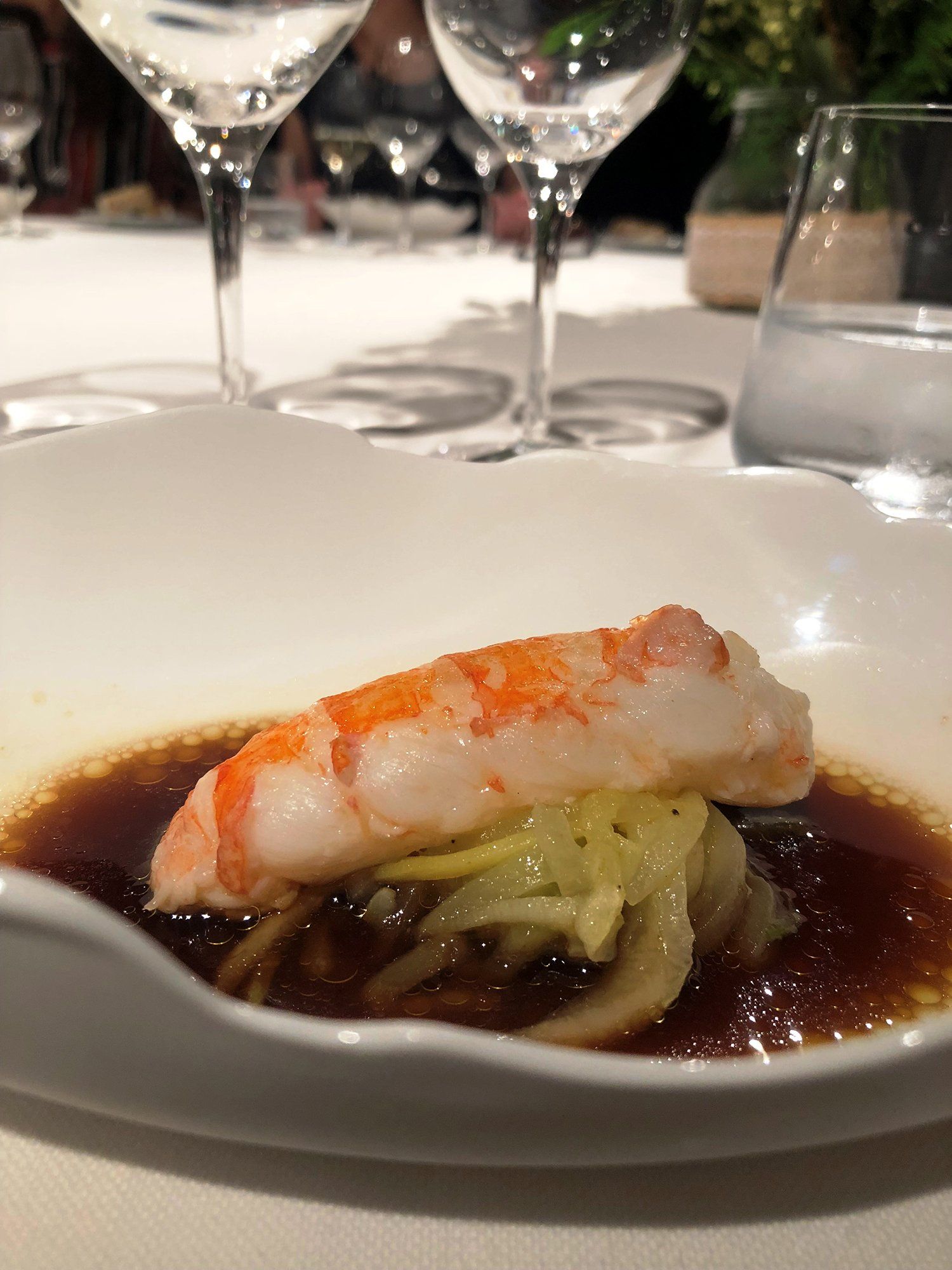 A close-up of a plate of food on a table with wine glasses in the background.