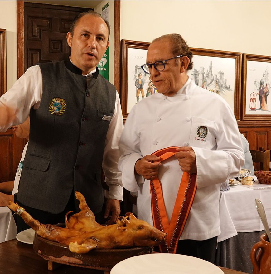 Two men are standing in front of a meat on a cutting board