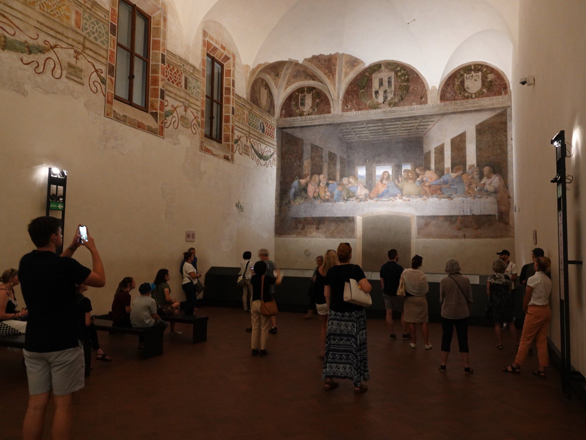 A group of people are standing in a room in front of a large painting.