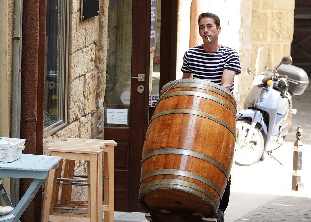 A man is pushing a large wooden barrel on a cart