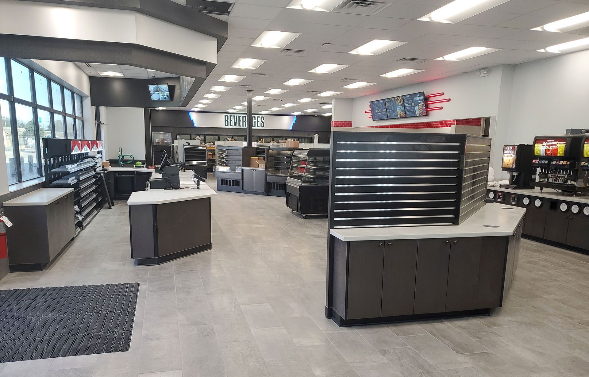 Interior view of a modern convenience store with various displays and merchandise. Brightly lit with gray floors and brown cabinetry.