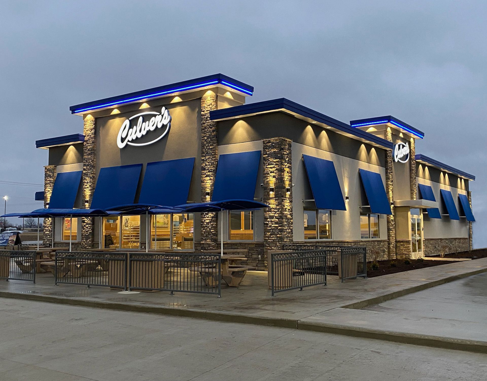 Culver's restaurant exterior with blue awnings, sign, and lights against an overcast sky.