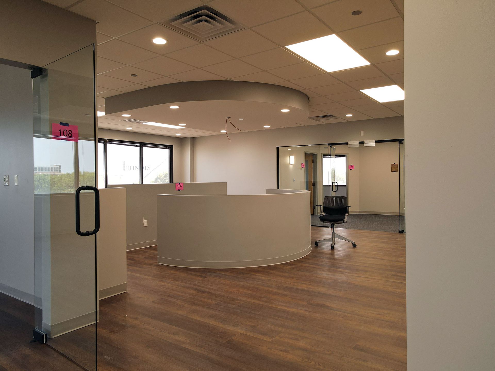 Empty office interior with curved reception desk and glass doors. Wood-look flooring and white walls.