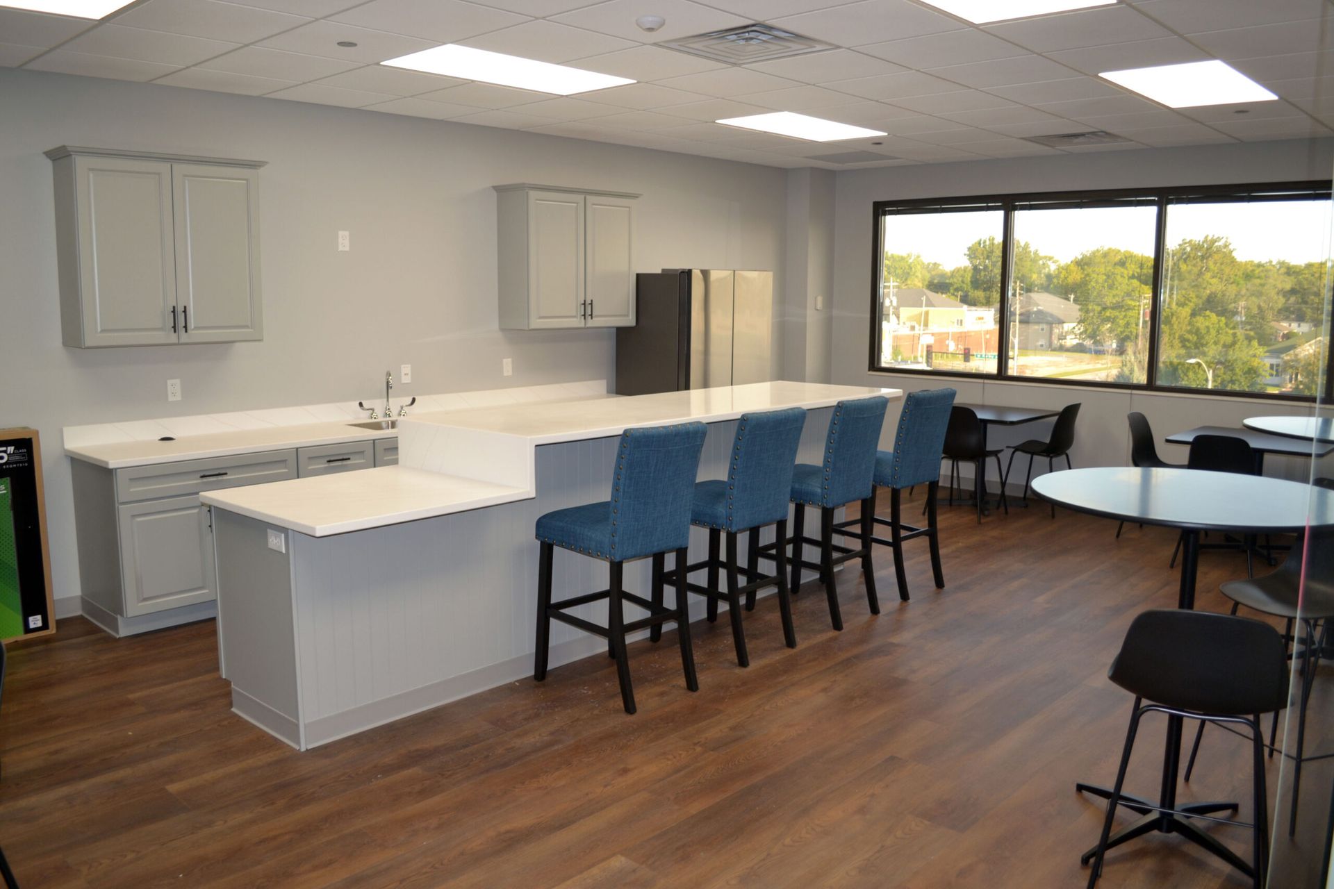 Kitchen and seating area with a large island, blue barstools, and a window overlooking trees.