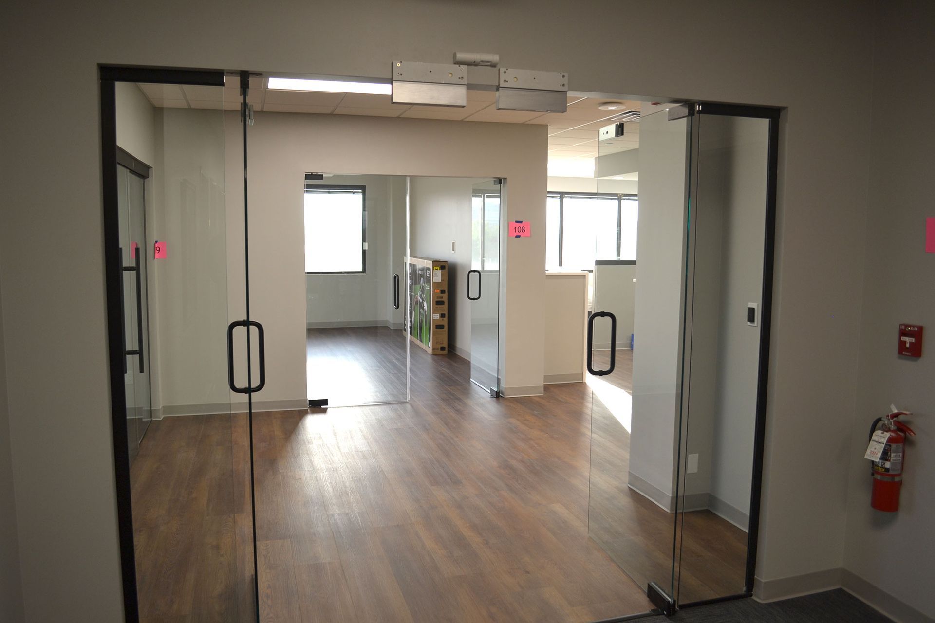Glass door entrance to office with wood floors, doors to the left, and windows in the background.