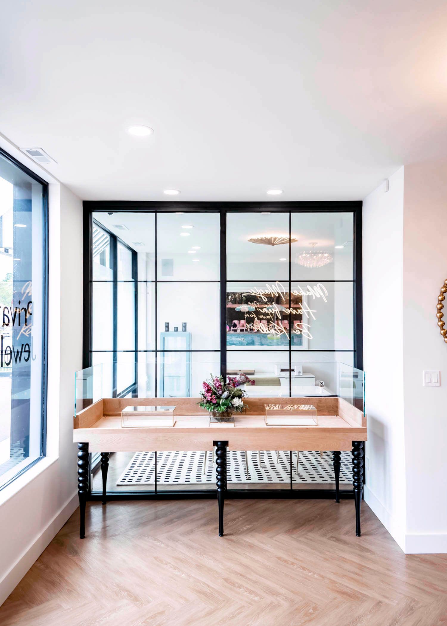 Entryway with wooden table, glass doors, and herringbone floor. White walls, black metal accents, and floral arrangement.