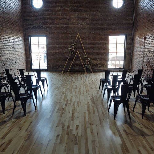 Empty event space with rows of black chairs, a wooden ceremony arch, and brick walls.