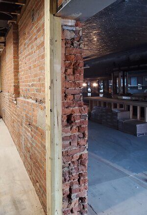 Brick wall with damaged section, wooden framing around doorway, interior view of a room.