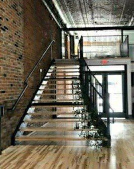 Staircase with wooden steps and metal railing in a brick-walled industrial-style building.