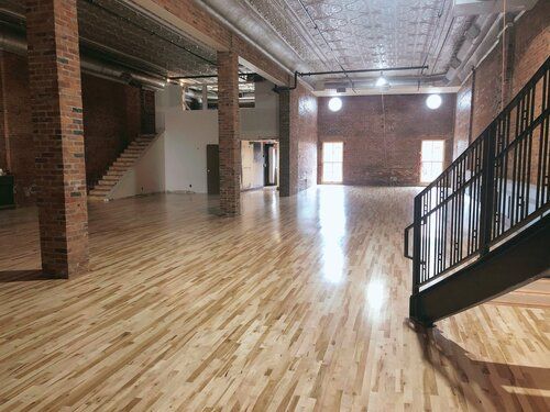 Large open room with wood floors, brick walls, a staircase, and support columns.