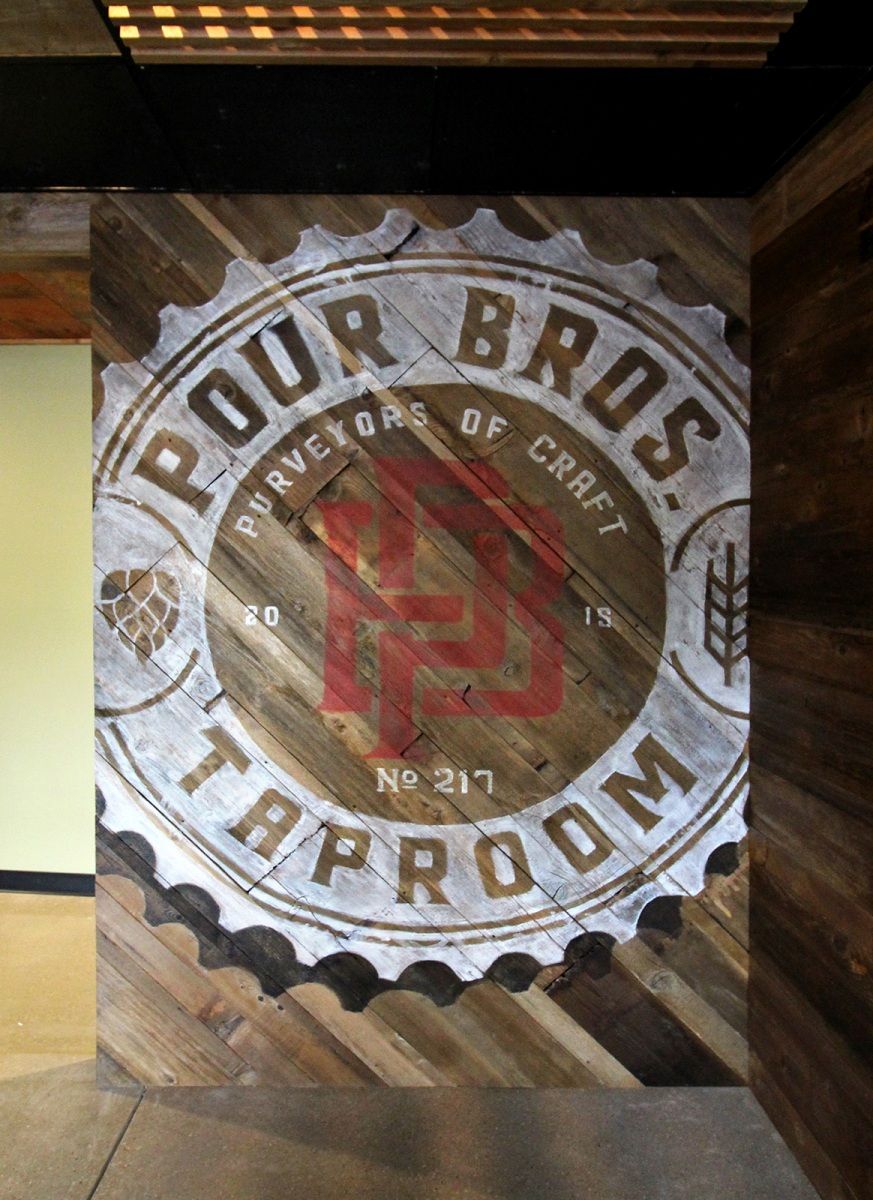 Pour Bros. Taproom logo on a wood-plank wall; white and red logo within a bottle cap design.