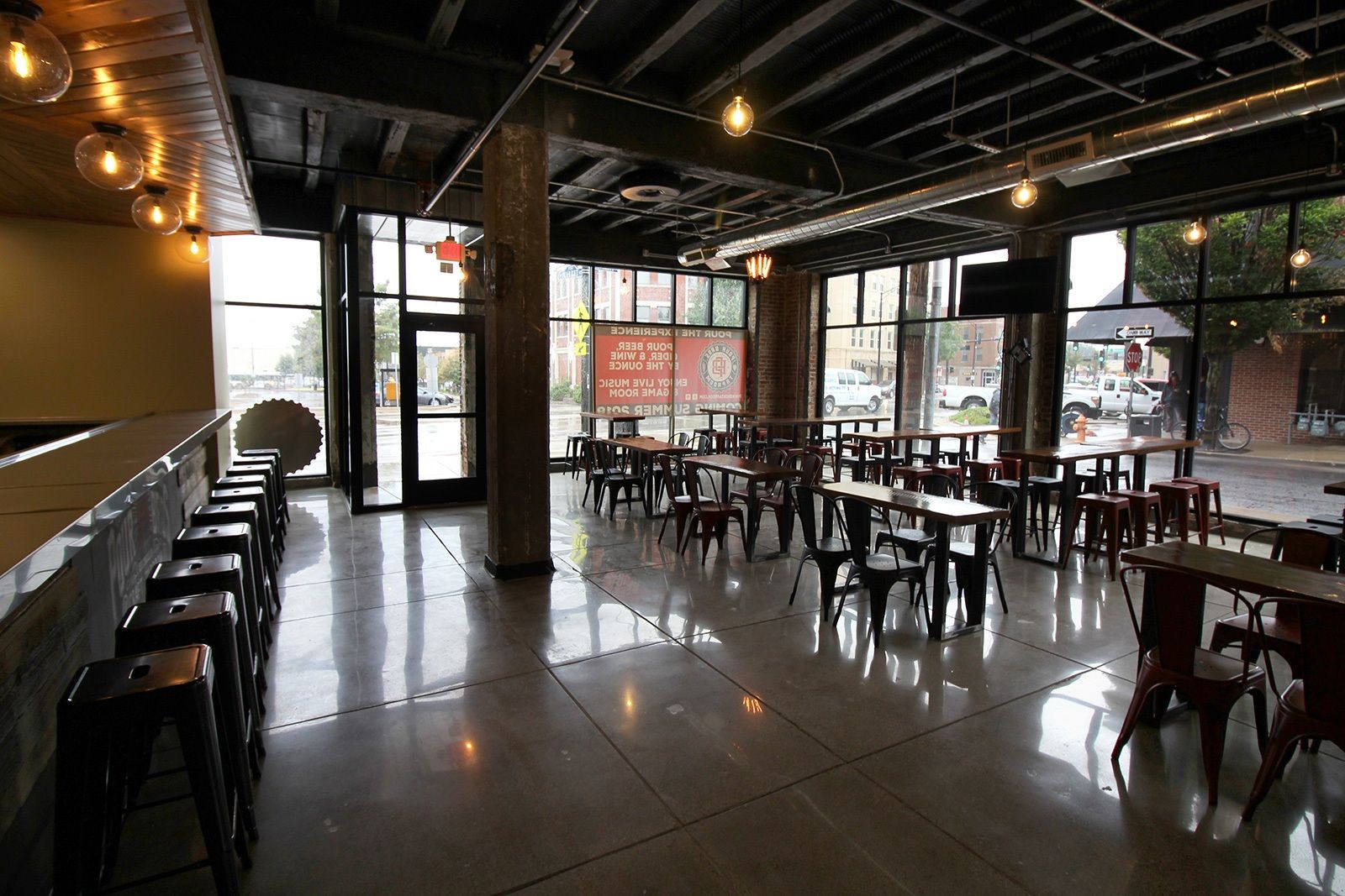 Empty restaurant interior with tables, stools, large windows, and exposed ceiling.