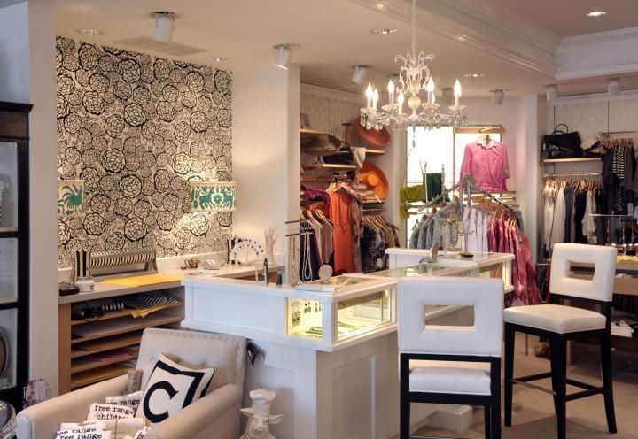 Boutique interior with clothing racks, a white counter, patterned wallpaper, and seating.