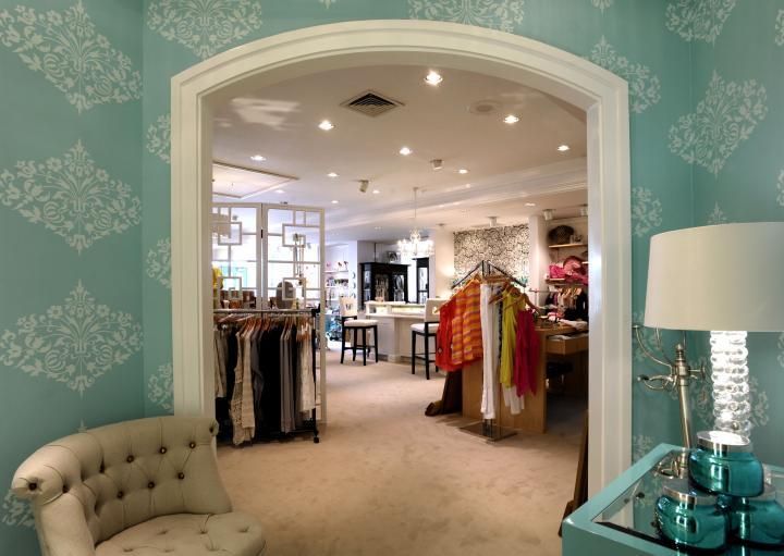 An arched doorway leading into a boutique. Teal walls with patterned wallpaper, a chair, and a lamp.