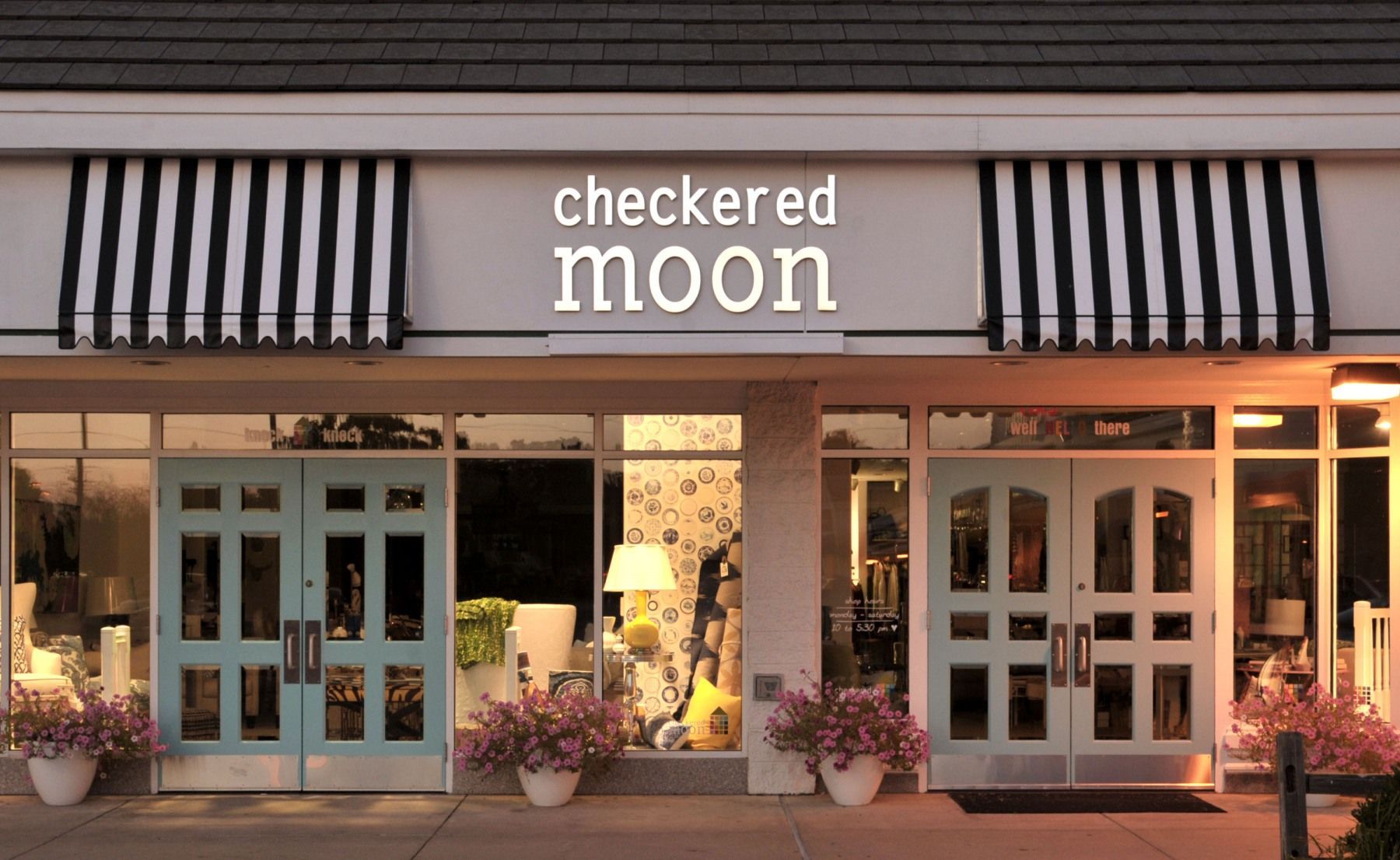 Checkered Moon storefront with turquoise doors, black/white striped awnings, and pink flower pots.