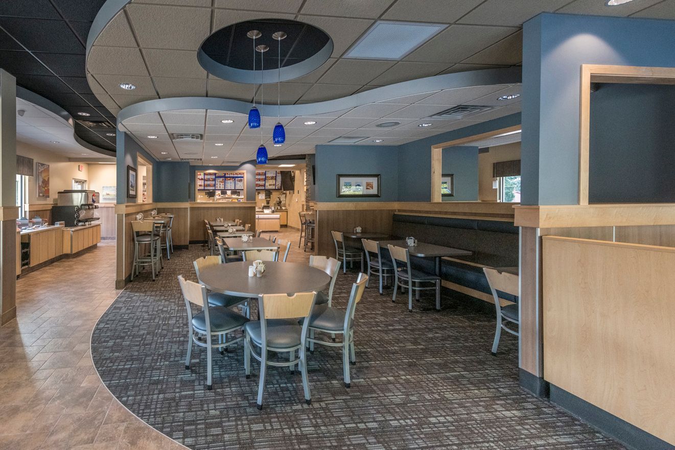 Restaurant interior with tables, chairs, and booths, featuring blue walls and accents, plus a curved ceiling.