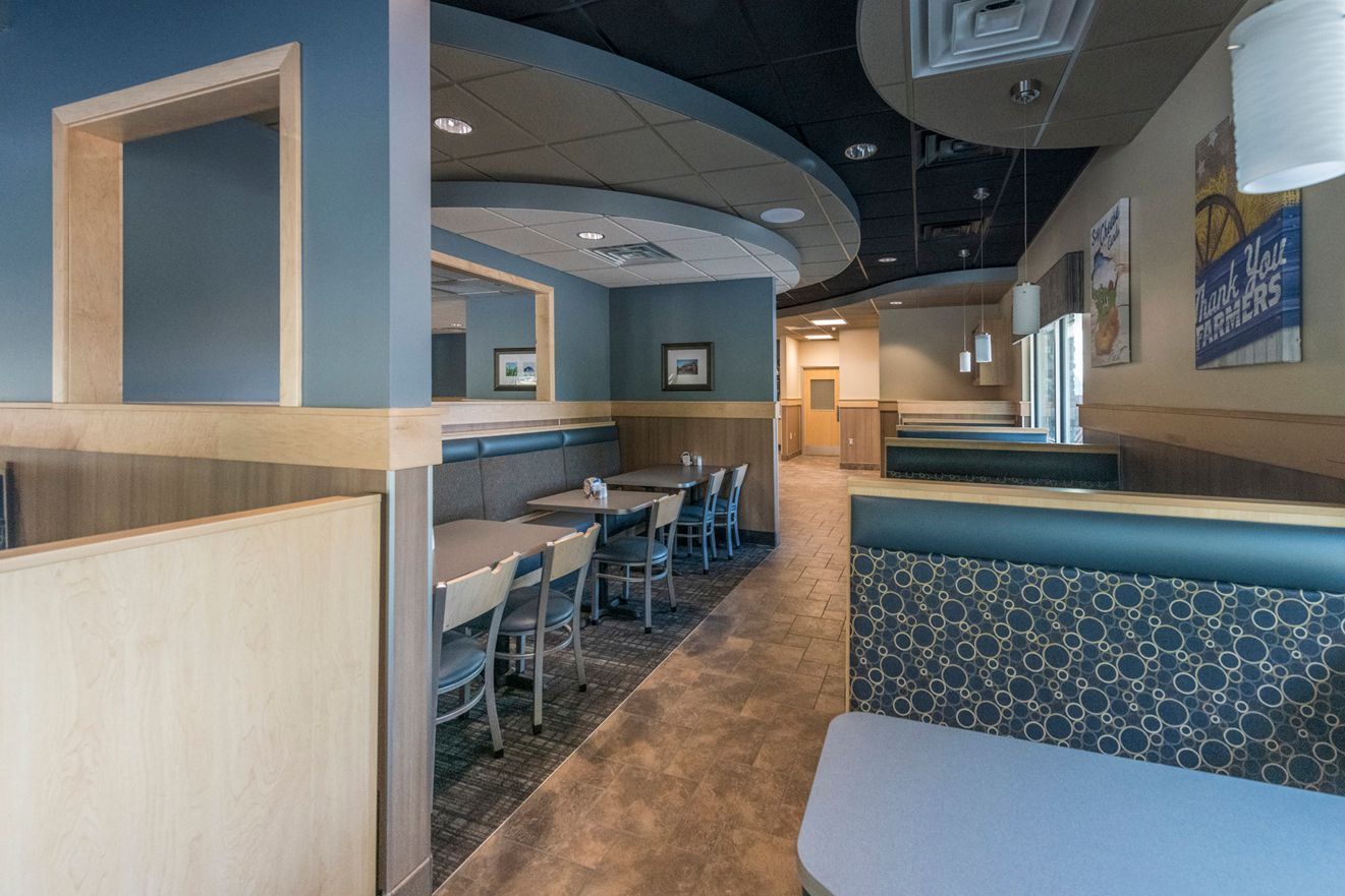 Restaurant interior: booths, tables, blue and beige walls, overhead lighting, view down a hallway.